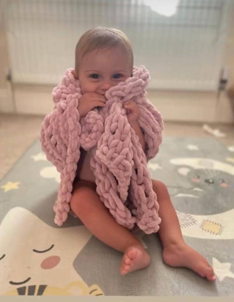 Baby wrapped in a pink hand knitted blanket on a play mat.